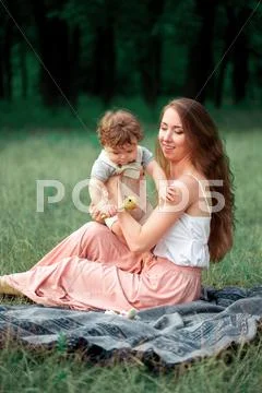 Young beautiful mother sitting with her little son against green grass. Happy Stock Photos