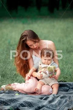 Young beautiful mother sitting with her little son against green grass. Happy Stock Photos