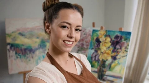 Young beautiful painter posing on camera staying near her masterpieces that she Stock Footage 74212849