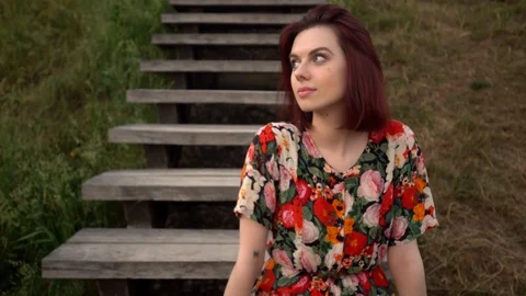 Young beautiful red-haired female sitting on wooden stairs in park Stock-Footage 109514341