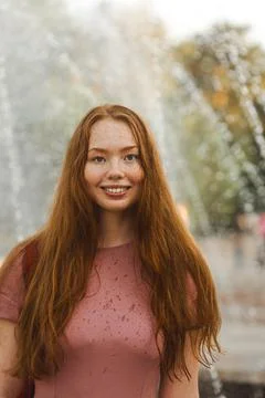 Young beautiful red-haired long-haired woman in a summer pink dress walks Stock Photos