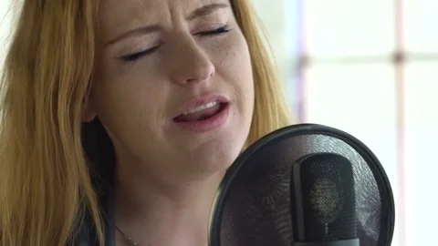 Young beautiful singer singing into the microphone at the studio, close-up Stock Footage 73688825