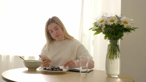 A young beautiful student has breakfast and keeps a creative journal. Stock Footage 272675559