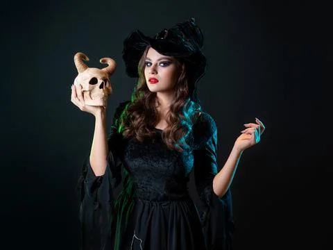 A young beautiful witch in a conical hat holds a devil's skull in her hands Stock Photos