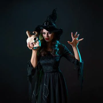 A young beautiful witch in a conical hat holds a devil's skull in her hands Stock Photos