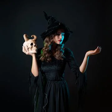A young beautiful witch in a conical hat holds a devil's skull in her hands Stock Photos