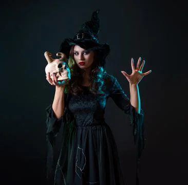 A young beautiful witch in a conical hat holds a devil's skull in her hands Stock Photos