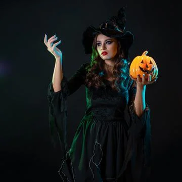 A young beautiful witch in a conical hat holds a Halloween pumpkin in her hands Foto stock