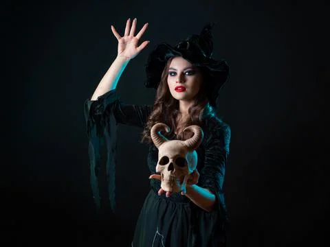 A young beautiful witch in a conical hat holds a devil's skull in her hands Stock Photos