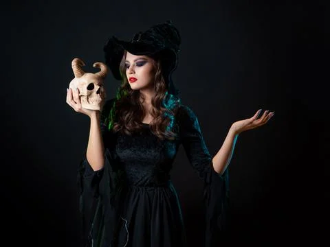 A young beautiful witch in a conical hat holds a devil's skull in her hands Stock Photos