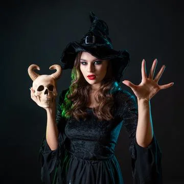 A young beautiful witch in a conical hat holds a devil's skull in her hands Stock Photos