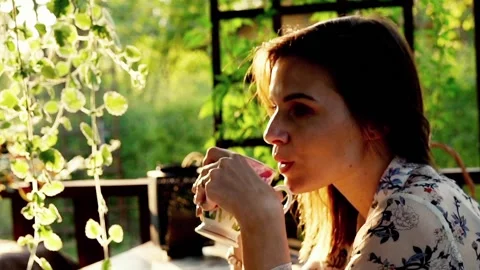 Young, beautiful woman drinking water on the porch in garden Stock Footage 129683553