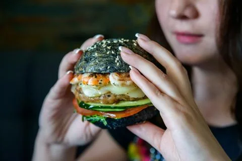 Young beautiful woman eats burger in restaurant Stock Photos