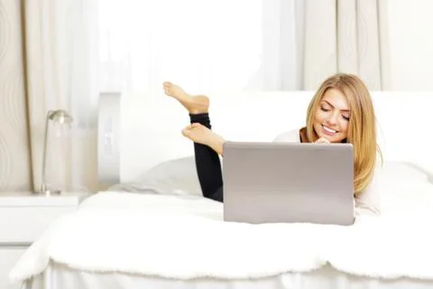 Young beautiful woman lying on the bed with laptop at home Stock Photos