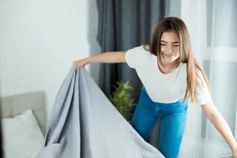 Young beautiful woman making her bed early in the morning looking happy Stock Photos