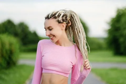 A young beautiful woman in a pink T-shirt with white dreadlocks outdoors. Stock Photos