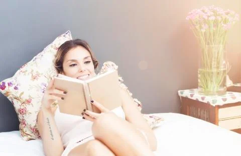 Young beautiful woman reading a book in bed Stock Photos