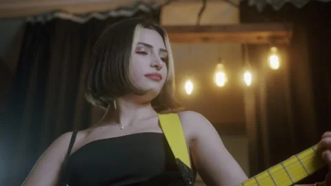 Young beautiful woman with short hair in a black dress plays the electric gui Stock Footage 145690003