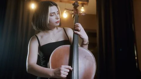 Young beautiful woman with short hair in black dress plays the cello in a mod Stock Photos