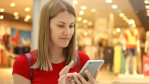 Young beautiful woman sitting in shopping mall smiling. Using her smartphone Stock Footage