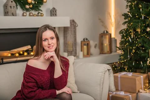 A young, beautiful woman is sitting on a sofa in a living room with a Christm Stock Photos