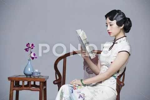 Young beautiful woman in traditional cheongsam reading book Stock Photos