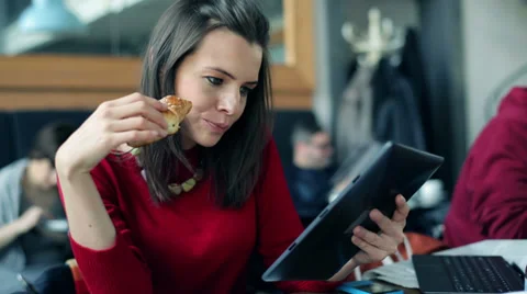Young, beautiful woman using tablet while eating croissant in the cafe Stock Footage 36645572