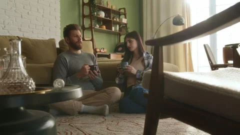 Young beloved couple sit on floor near couch chatting at home Video stock 266801416