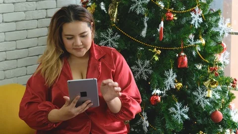 Young big size or plus size girl enjoys online shopping on tablet on Christmas Stock Footage 120727302