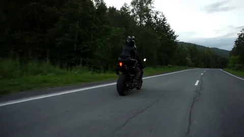 A young biker in a leather jacket and a helmet riding at the motorcycle along Stock Footage 83484936