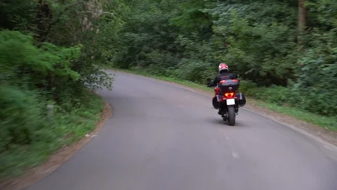 Young biker riding motorcycle through forest road. Steady gimbal shot. 4K. Video stock 111617320