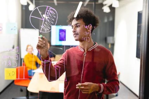 Young biracial male app developer drawing chart on glass in board room Stock Photos