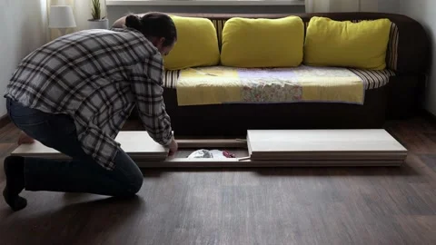 Young Black Bearded Long-haired Man Lays Out Parts Of Bookcase On Floor For Stock Footage 169717606