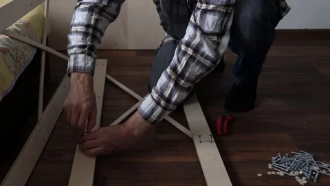 Young Black Bearded Long-haired Man Lays Out Parts Of Bookcase On Floor For Stock Footage 169718029