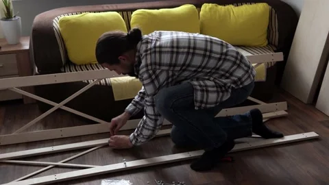Young Black Bearded Long-haired Man Lays Out Parts Of Bookcase On Floor For Stock Footage 169718804