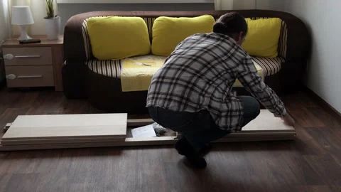 Young Black Bearded Long-haired Man Lays Out Parts Of Bookcase On Floor For Stock Footage 169719086