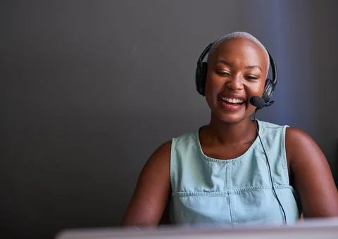 A young Black call centre agent laughs while on a call with headset Stock Photos