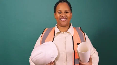 Young Black construction worker smiling holding hard hat, working on site Stock Photos