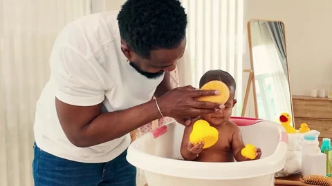 Young Black father lovingly bathes his baby daughter in a white tub. 스톡 동영상 308510568