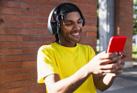 Young black guy with helmets smiling while acting with cell phone on the stre Foto stock