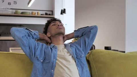 Young black guy student in blue shirt sitting on sofa at home in modern interior Stock Footage 142605348