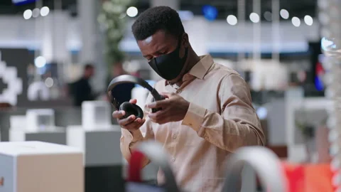 Young black guy is viewing new model of wireless headphones in trading hall of Stock Footage 153072854