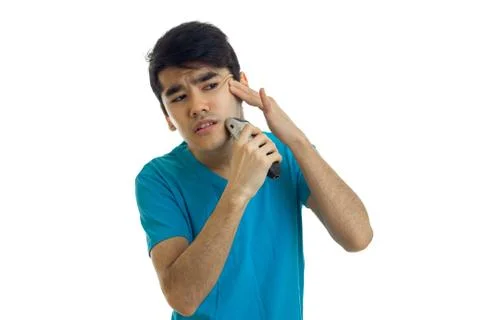 A young black-haired guy in a blue t-shirt looks away and shaves Stock Photos