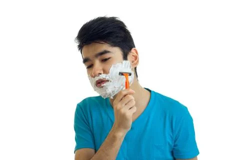 Young black haired guy lowered his head down and shaves his beard with a razor Stock Photos