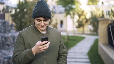 Young black haired guy texting in a park Stock Footage 79572403