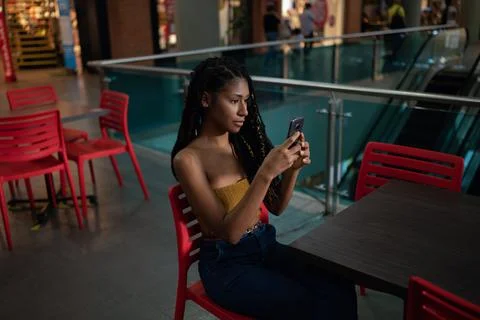 Young black latin woman uses smart phone in commercial mall Stock Photos