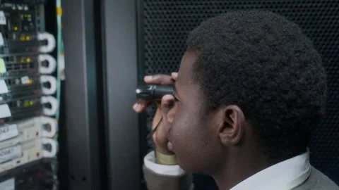 Young Black Male IT Engineer Examining Hardware in Data Center with Flashlight Video stock 303554004