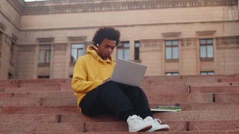 Young black male programmer in casual clothes sitting outdoors on stairs and Stock Footage 276426488
