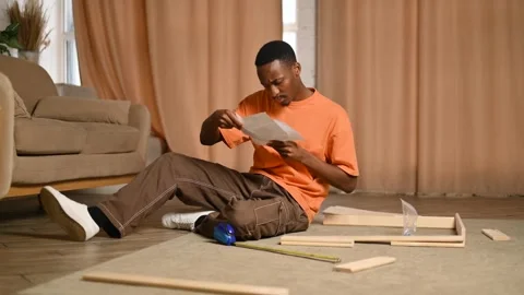 Young black man assembling a rack according to instructions Stock Footage 275201382