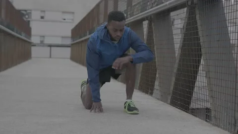 Young black man in a blue jacket ties his shoe on a bridge Vídeos de archivo 146960433